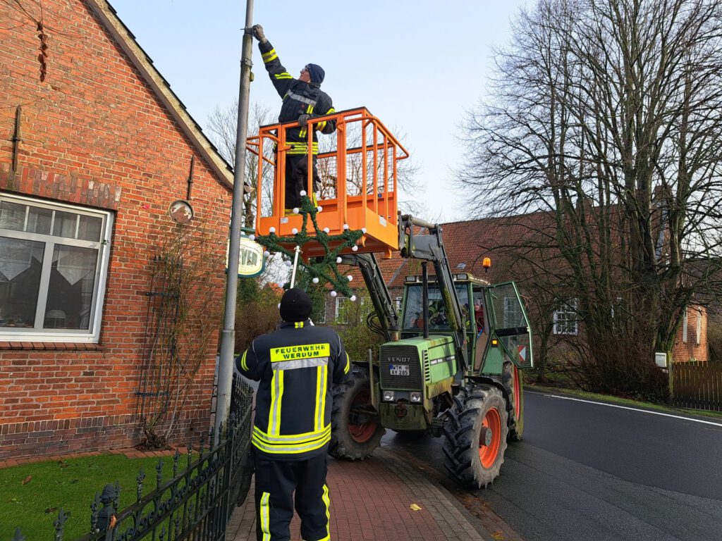 Sebastian Post ist mit dem Frontlader vorgefahren. Oben bereitet Anne Osterkamp die Halterung am Mast vor und Thomas Jakobs reicht schon mal das Beleuchtungselement zu 